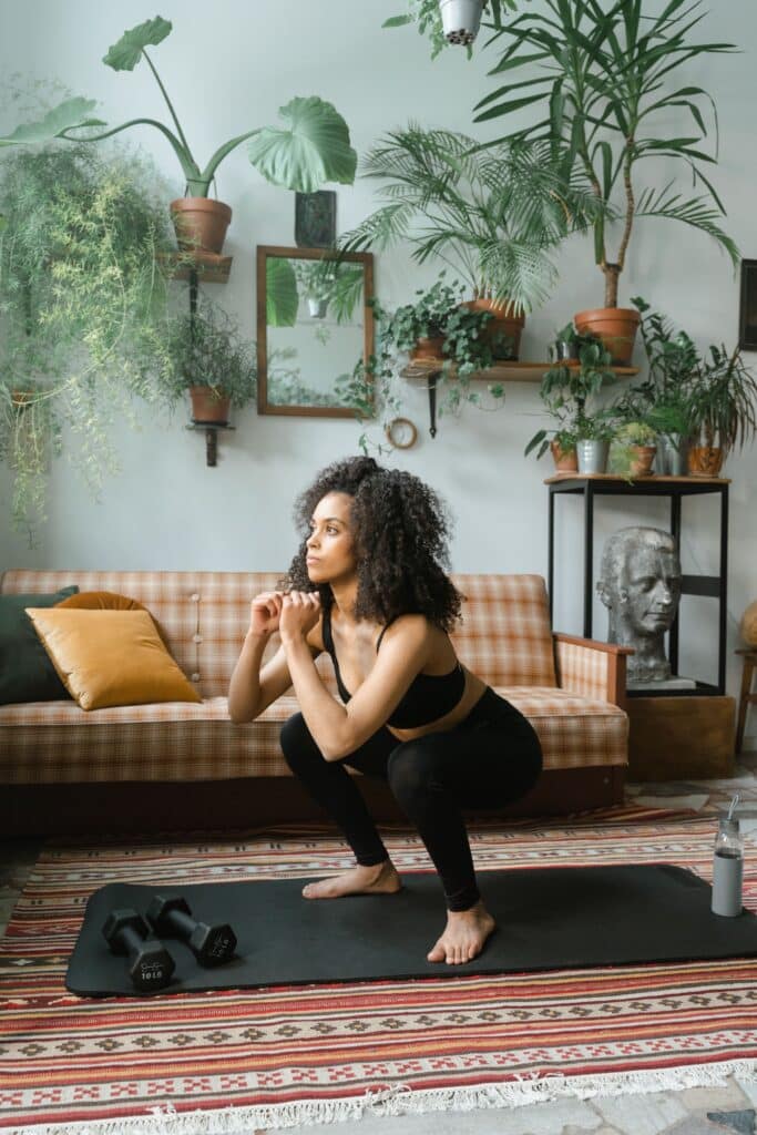 Dame laver squats på en yogamåtte i hendes hjem.
