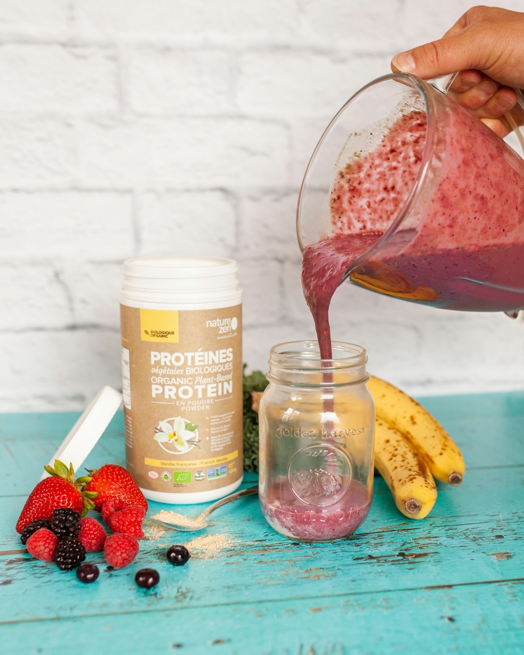 Smoothie der hældes op i et glas med frugter rundt omkring.